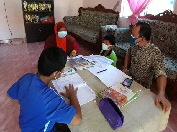 Maszlee (kanan) melihat satu keluarga yang menjalani PdPR sewaktu melawat kawasan Felda Ayer Hitam di Simpang Renggam, Kluang pada Ahad.