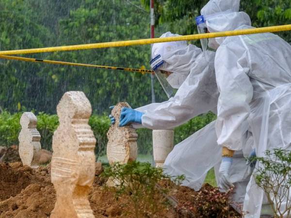 Petugas pasukan pengurusan jenazah Unit Kecil Perkuburan Taman Selatan Putrajaya membantu seorang ahli keluarga jenazah pesakit Covid-19 meletakkan batu nisan di Tanah Perkuburan Islam Taman Selatan Putrajaya. - Foto Bernama