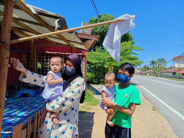 Salmizan bersama anak lelaki dan kembarnya di hadapan rumah sewa mereka di Kampung Gelang Mas, Pasir Mas mengibarkan bendera putih.