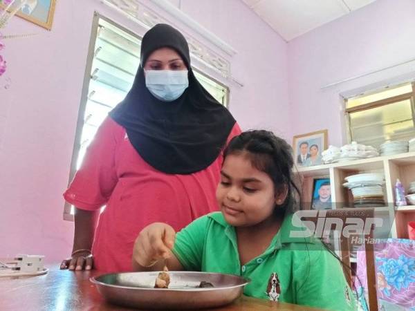 Hamidah melihat anak bongsunya makan makanan yang diberikan jiran ketika kunjungan pemberita di kediamannya pada Khamis.