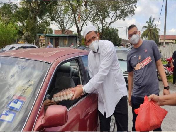 Mohd Jazri (kanan) bersama Nabil menyerahkan bakul makanan kepada penerima secara pandu lalu di hadapan Surau Taman Menara Maju.