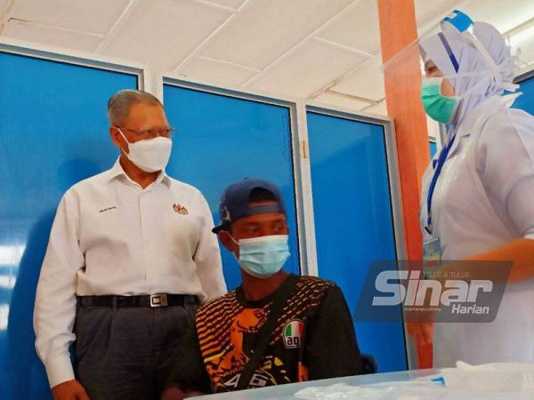 Mustapa (kiri) meninjau proses suntikan Covid-19 salah seorang masyarakat orang asli di Program Outreach Vaksinasi di Dewan Serbaguna Kampung Sungai Rual, Jeli pada Sabtu.