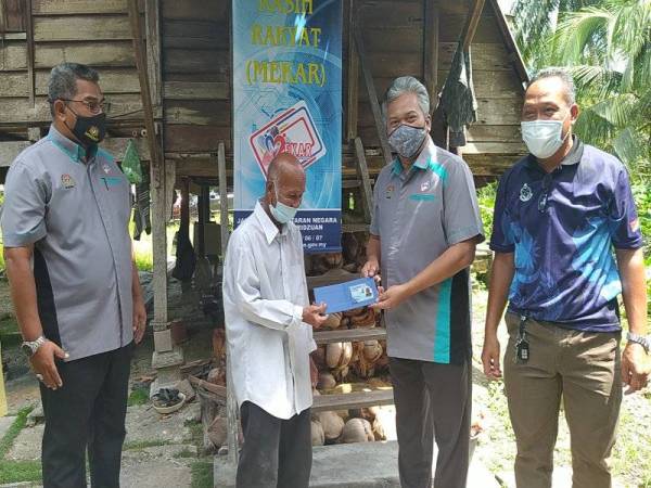 Saiful Yazan (dua dari kanan) menyerahkan MyKad kepada Mat Sani di rumahnya di Kampung Parit Haji Tahir di sini pada Rabu.