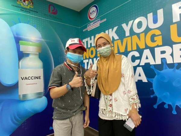 Delailah (kanan) mengiringi Mohamad Iqbal yang teruja menerima vaksin di PPV Hospital Pakar KPJ Johor, Johor Bahru pada Selasa.