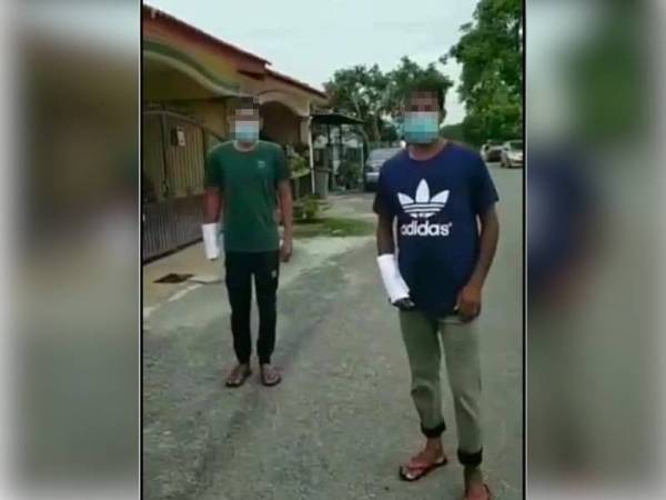 Tangkap layar video dua lelaki warganegara asing memakai gelang berwarna merah jambu menutup lengan mereka dengan kertas putih.