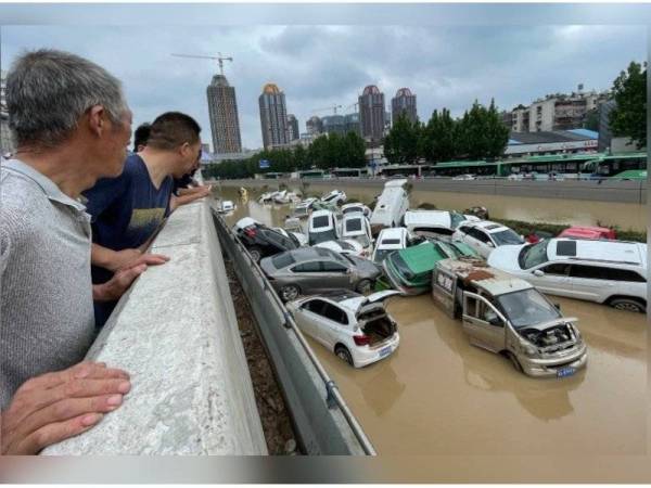 Gambar fail menunjukkan beberapa orang menyaksikan puluhan kenderaan bertindih akibat banjir yang berlaku pada Selasa lalu di bandar raya Zhengzhou. - Foto AFP