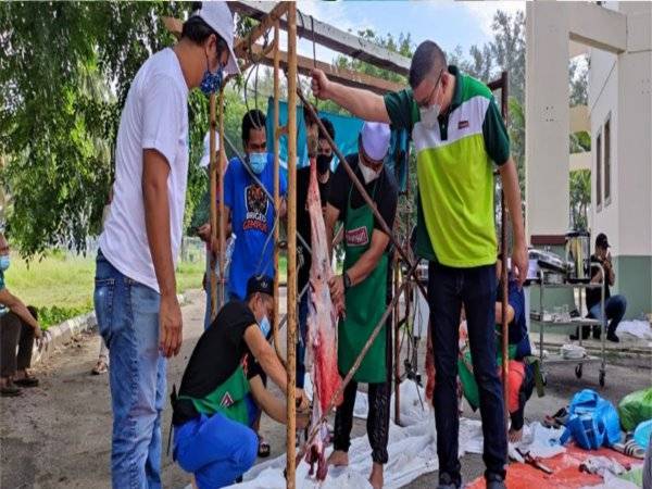 Mohd Jazri (kanan) membantu petugas melapah lembu korban sebelum dagingnya diagihkan kepada penerima.