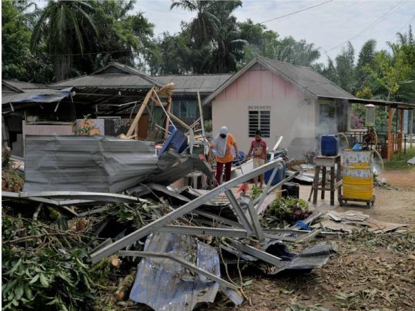 Mastura Abidin, 50, dibantu anak lelakinya, Mohd Fahrin mengemas dan membersihkan kedai mereka yang rosak dihempap pokok yang tumbang akibat ribut pada Jumaat di Kampung Teluk Jeri Luar,Tanjung Sedili. - Foto Bernama