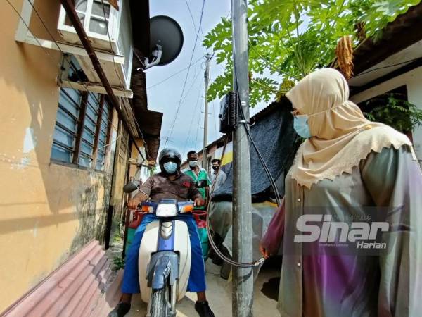 Hamidah (kanan) melihat tiang gentian optik yang dipasang di tengah lorong belakang rumah di Taman Perpaduan di sini yang menyebabkan laluan itu terhalang dan sempit.