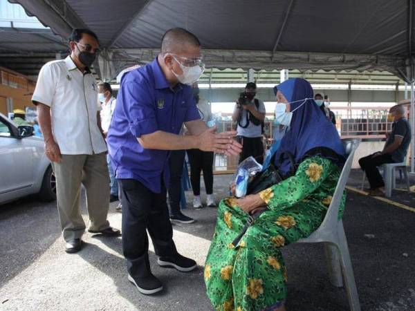 Saarani menunjukkan penjagaan kebersihan tangan kepada seorang warga emas ketika lawatannya ke Program Outreach Vaksinasi Dewan Undangan Negeri (DUN) Batu Kurau di Dewan Astaka Batu Kurau.