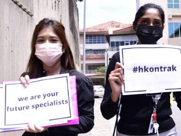 Dua wanita dipercayai pegawai perubatan berstatus kontrak hadir membawa plakad di pekarangan Hospital Queen Elizabeth 1, Kota Kinabalu pada Isnin.