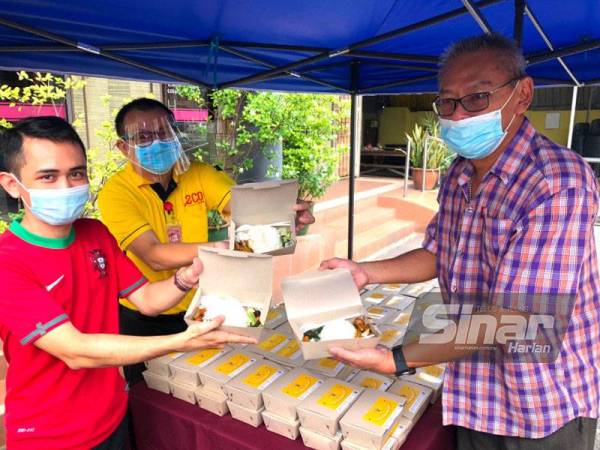 Swim Him (kanan) dan Pooi Shin (dua dari kiri) menunjukkan kotak nasi yang diagihkan secara percuma di hadapan Restoran Sri Chengmai di Sri Cemerlang pada Khamis.
