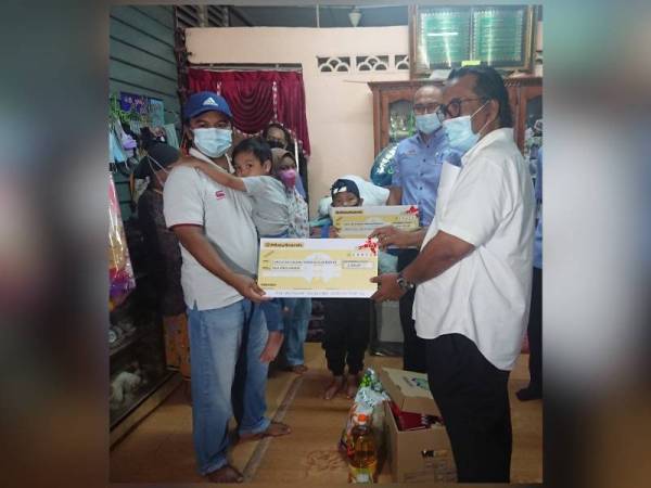 Mohamad Shukri (kiri) menerima replika cek bayaran Faedah pengurusan Mayat yang disampaikan oleh Ismail di Kampung Air Hitam Darat, di Masjid Tanah, di sini, pada Khamis.