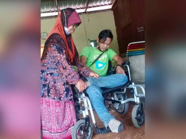 Tom membantu anaknya, Abdul Malik menaiki kerusi roda di rumah mereka di Kampung Baru, Pendang.