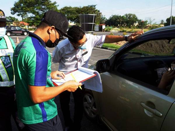 Pegawai Kesihatan Daerah Pendang, Dr Mohd Lutpiyudin (kanan) bertanyakan sesuatu kepada penerima vaksin pada aktiviti pemberian vaksin pandu lalu di taman permainan dan rekreasi Pendang, hari ini.