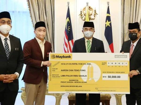 Mohd Ali (tengah) menyaksikan replika cek RM50, 000 yang disampaikan Sulaiman (kanan) kepada Aaron Chia di pejabat Yang Dipertua Negeri di Ayer Keroh, di sini, pada Rabu.