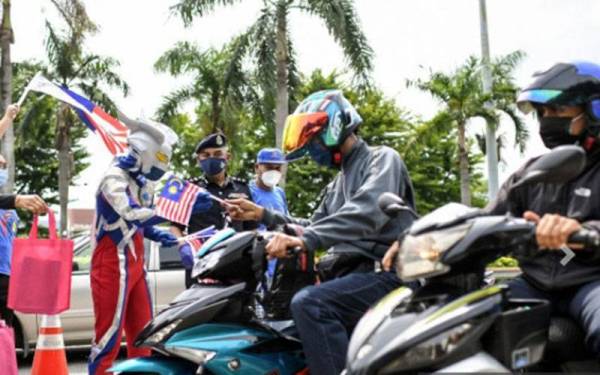 Soffian bersama Mohamad Syukur yang mengenakan kostum karakter adiwira 'Ultraman' pada program penyerahan Jalur Gemilang kepada pengguna jalan raya anjuran Jabatan Penerangan Pulau Pinang di sekatan jalan raya di Lebuhraya Tun Dr Lim Chong Eu, Georgetown hari ini.  