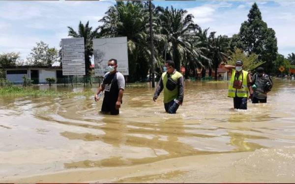 Penduduk berjalan mengharungi banjir untuk keluar ke kawasan pekan berhampiran. 