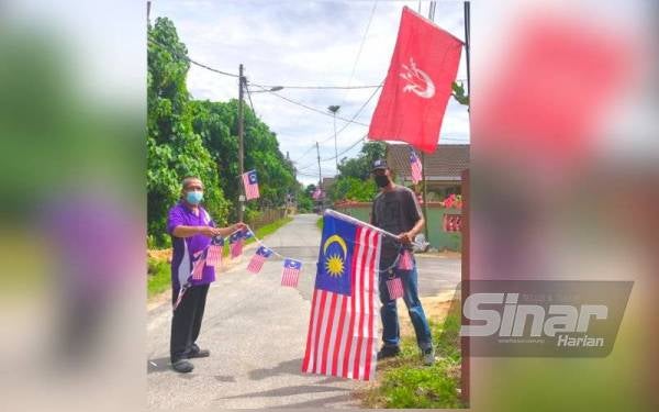 Pengerusi Pertubuhan Kebajikan Penduduk Mukim Parit, Wan Azizi Wan Ab Ghani (kanan) dan penduduk, Tuan Mohd Nor Tuan Yahya,56, membetulkan bendera Malaysia untuk digantung pada tiang-tiang elektrik di laluan utama kampung-kampung di Mukim Parit, Pasir Tumboh.