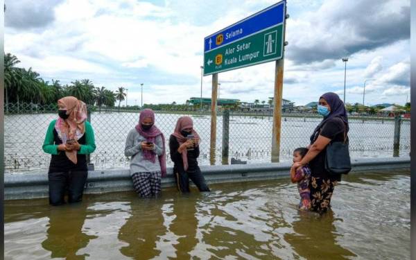 Masyarakat setempat berehat di pembahagi jalan ketika melalui jalan yang dinaiki air ekoran kejadian ban pecah dan hujan lebat, ketika tinjauan Bernama di sekitar kawasan Jalan Alor Pongsu-Selama dan Kampung Parit Simpang 5. - Foto Bernama