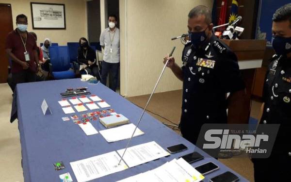 Ayob Khan menunjukkan surat Kementerian Perdagangan Antarabangsa dan Industri serta surat pengesahan majikan yang palsu dan barang-barang dirampas daripada sindiket ah long pada sidang akhbar di IPK Johor, Johor Bahru pada Isnin.