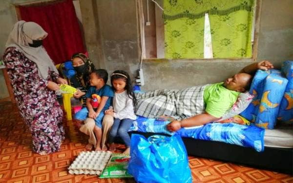 Che Norhayati (kiri) daripada NGO Cempaka Merah Asnaf Solution menyampaikan zakat kepada Mohammad Rosli sekeluarga bagi meringankan beban mereka.