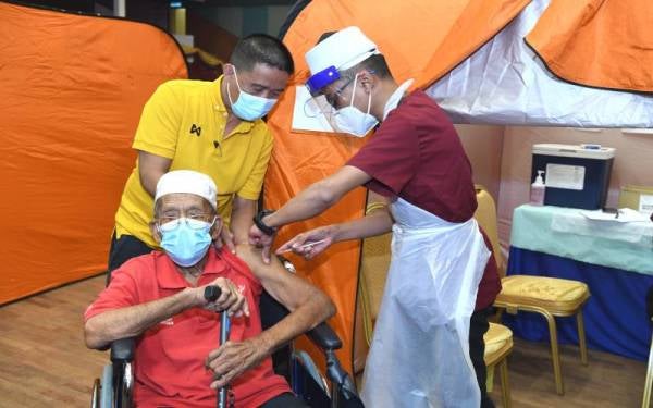 Che Ismail ditemani cucunya, Mohd Jailani (kiri) ketika menerima suntikan pertama Covid-19 di PPV UniSZA pada Rabu.