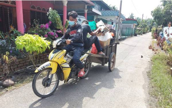 Penduduk menaiki motosikal membawa sampah dan peralatan rumah yang rosak akibat banjir untuk dibuang.
