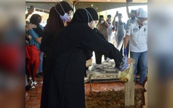 Isteri Allahyarham, Normilah menyiram pusara suaminya selepas selesai upacara pengebumian di Taman Perkuburan Orang-orang Islam Kampung Kebatu dan Kampung Kabidang, Beaufort.