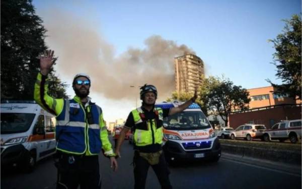 Sebuah bangunan apartmen (di belakang anggota-anggota polis) terbakar di Milan, Itali pada Ahad. - Foto AFP