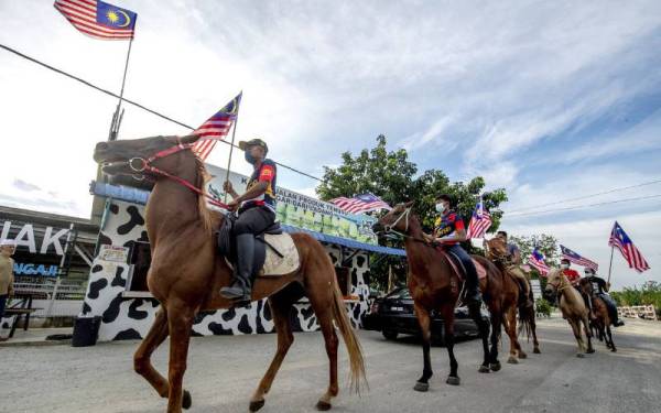 Nik Syazwan (kiri) bersama rakan menunggang kuda sambil kibarkan Jalur Gemilang sempena sambutan Bulan Kebangsaan 2021 ketika ditemui Bernama di Ladang SRZ Ternak Ladang Tenusu, Jeram Mengaji, Pasir Puteh, Kelantan. - Foto Bernama