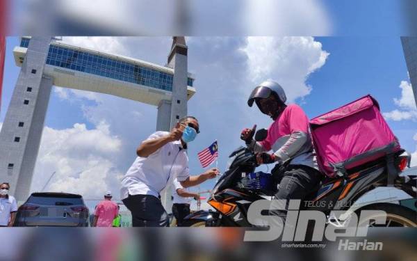 Tun Ahmad Faisal memasang bendera pada motosikal seorang penghantar makanan yang melalui Drawbridge pada Isnin.