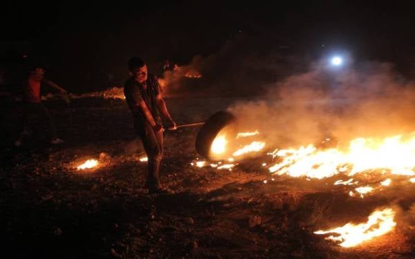 Seorang penunjuk perasaan Palestin membakar tayar semasa pertempuran dengan tentera Israel. Foto Xinhua