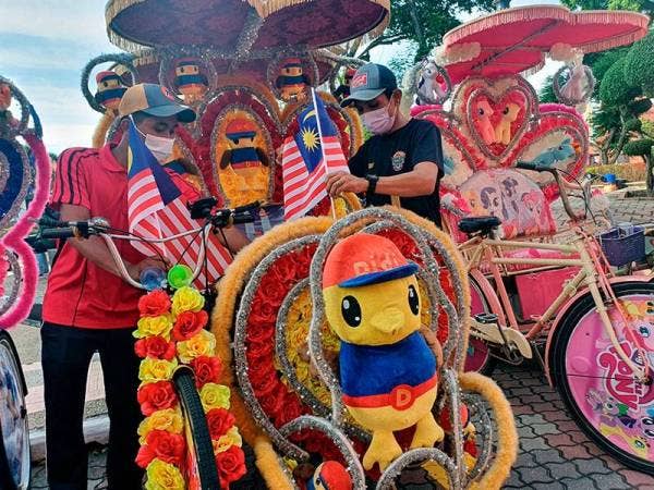 Pengayuh beca Mohd Azuan Abdul Shukor, 34, (kanan) dan Zulhairie Abdullah, 21, sedang menghias Jalur Gemilang di beca sempena sambutan Hari Kebangsaan ke-64 pada sesi penyerahan Jalur Gemilang kepada Pengayuh Beca di Bandar Hilir hari ini.