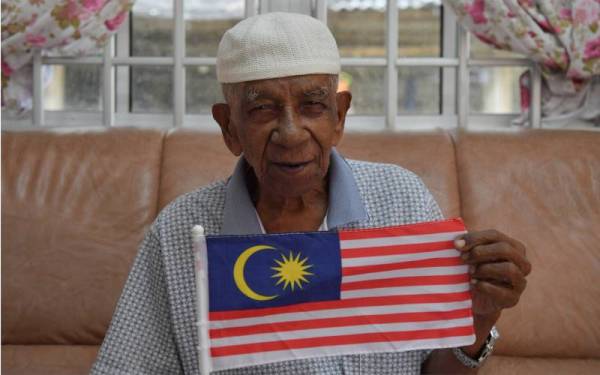 Abdullah memegang Jalur Gemilang ketika menceritakan detik bersejarah pada tahun 1957 di Taman Sri Penunjuk, Kijal. -Foto Bernama