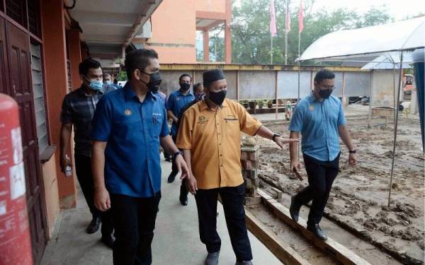Mohd Radzi (dua dari kiri) diiringi Guru Besar Sekolah Kebangsaan Haji Nyak Gam, Mohd Rosli Hassan (dua, kanan) melawat sekitar sekolah yang rosak selepas dinaiki banjir lumpur ketika melawat ke sekolah itu pada Sabtu. - Foto Bernama