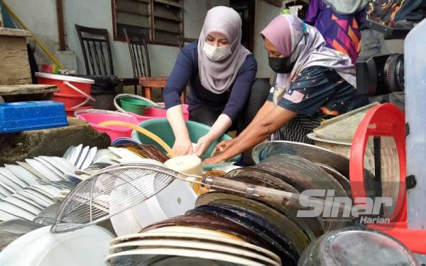 Rina membantu membersihkan pinggan mangkuk yang terjejas akibat tragedi kepala air di rumah Sukiena Abu Bakar (kanan) di Jalan Masjid Yan pada Sabtu.