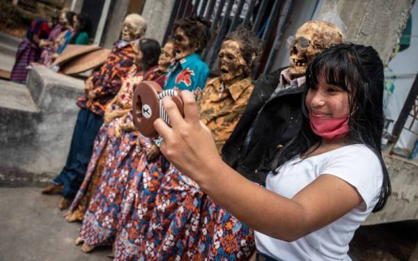 Seorang gadis bergambar dengan mayat-mayat yang dikumpulkan di rumah adat Tongkonan di mana semua waris si mati berhimpun. - AFP