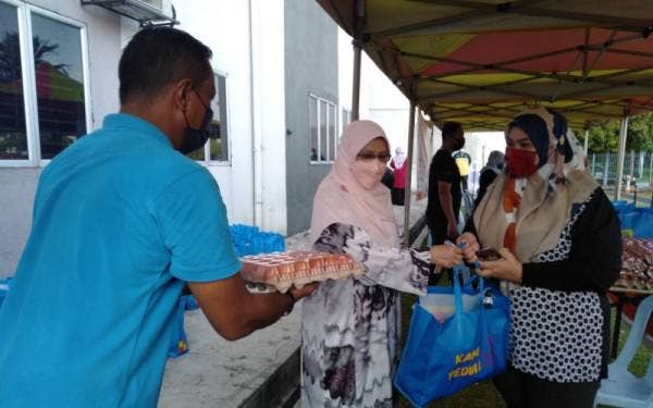 Rodziah (dua dari kiri) menyerahkan barangan keperluan asas kepada salah seorang penduduk di PPR Hicom, di Shah Alam pada Ahad.