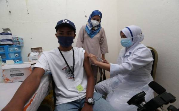 Siti Rohana Idris,41, (tengah) bersama anak sulungnya, Ahmad Airoul Firhan Mohd Rosdi, 18, (kiri) yang hadir bagi mendapatkan suntikan vaksin Covid-19 di Pusat Pemberian Vaksin (PPV) di Dewan Kopeladar Wakaf Bharu, Tumpat pada Rabu.