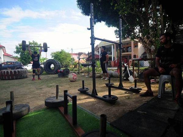 Peminat sukan bina badan Muhammad Haniff Mustafa 28 (kiri) bersama rakan melakukan aktiviti angkat berat di laman rumahnya ketika tinjauan di Puncak Alam hari ini.