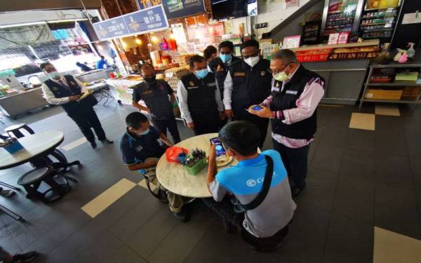 Veerapan (dua dari kanan) melihat Mohammad Faid (kanan) memeriksa kad suntikan vaksin seorang pelanggan di sebuah restoran.

