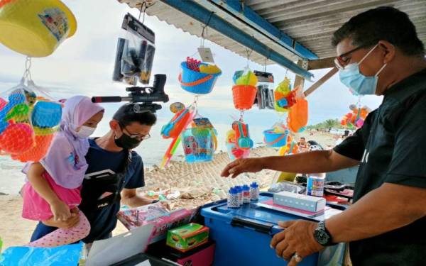 Zainal (kiri) melihat peralatan mainan pantai yang dijual di gerai Suhaimi ketika mengunjungi Pantai Ban Pecah, Tanjung Piandang di sini.