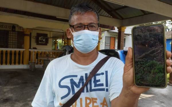 Yahya menunjukkan gambar keadaan tali air berdekatan rumahnya yang berminyak dan berbau busuk di Kampung Baru Sri Aman, Seelong Kempas pada Rabu.