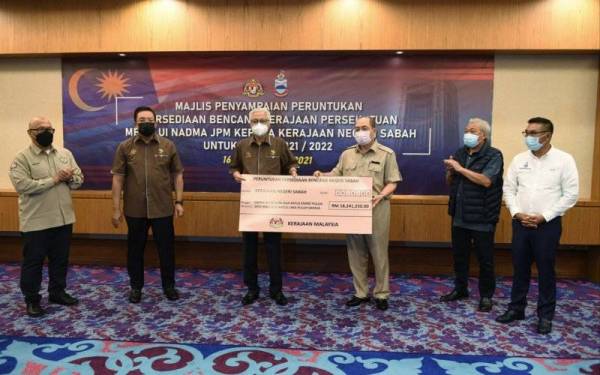 Perdana Menteri Datuk Seri Ismail Sabri Yaakob (tiga, kiri) menyampaikan replika cek bernilai RM18,241,250 kepada Ketua Menteri Sabah Datuk Hajiji Noor (tiga, kanan) pada majlis penyampaian peruntukan persediaan bencana kerajaaan persekutuan melalui Nadma Jabatan Perdana Menteri kepada kerajaan negeri Sabah untuk 2021/2022 di Menara Kinabalu hari ini. Turut sama Timbalan Ketua Menteri Sabah Datuk Seri Bung Moktar Radin (dua, kanan) dan Ketua Setiausaha Negara Tan Sri Mohd Zuki Ali (dua, kiri). - Foto Bernama