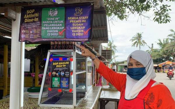 Napisah menunjukkan papan tanda di gerainya yang perlu dipatuhi pelanggan di Pantai Cahaya Bulan (PCB) di Kota Bharu pada Khamis.