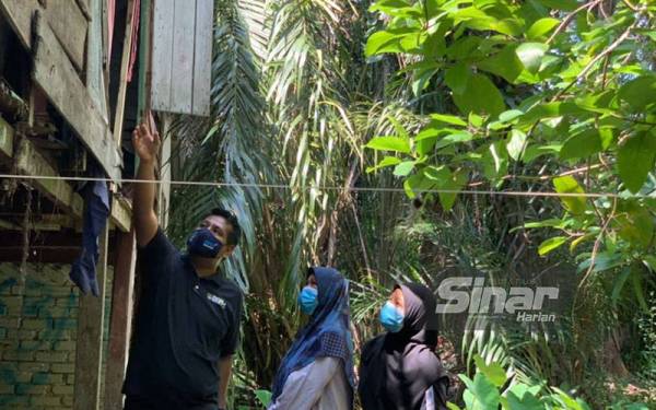 Khairul Shahril (kiri) melihat dinding rumah Ramlah (tengah) dan anaknya, Ruziah yang reput dan rosak di Kampung Lambor Kanan.