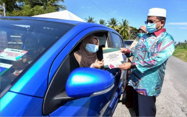 Ahmad Marzuk (kanan) menyampaikan sumbangan kepada sebahagian penerima secara pandu lalu pada Majlis Penyampaian Sumbangan Pelajar Baharu IPT di Pusat Khidmat Ahli Parlimen Pengkalan Chepa, Kota Bharu pada Sabtu. - Foto Bernama