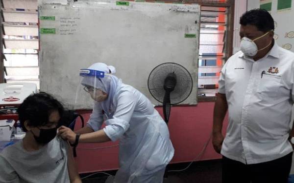 Mazlan (kanan) melihat seorang pelajar diberikan suntikan sempena Program Imunisasi Kebangsaan Bagi Vaksinasi Pelajar Sekolah Negeri Johor di Sekolah Menengah Kebangsaan (SMK) Taman Daya, Johor Bahru, pada Isnin.