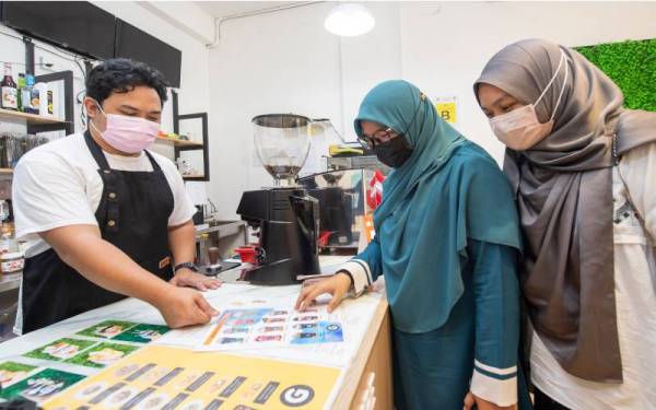 Wan Mohd Azizul Solehin (kiri) melayani pelanggannya di kafenya di Pasir Pekan di sini. - Foto Bernama 